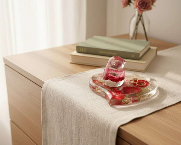 Rose heart trinket dish in clear glossy resin with red and pink pressed roses, green botanicals, gold leaf, and a matching rose-filled songbird.