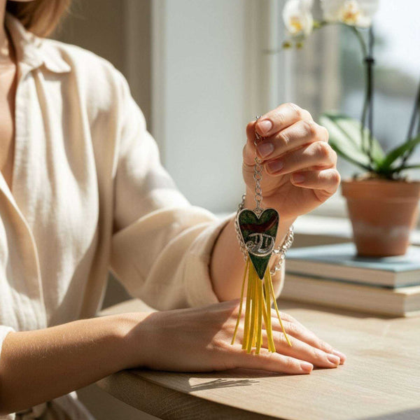 Antique silver sloth heart bag charm featuring a silver sloth hanging from a branch against a green botanical background with a bright yellow tassel.