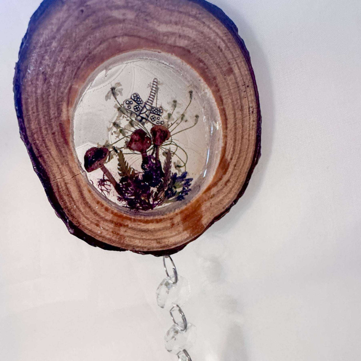 Suncatcher with a natural bark-edged wood slice, clear resin forest scene of mushrooms and botanicals, and hanging crystal