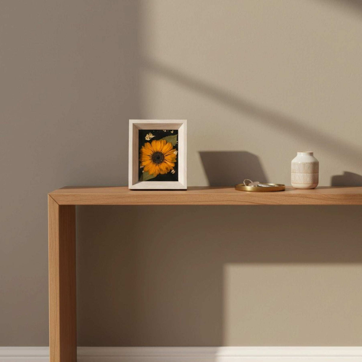 Pressed sunflower frame art with an orange bloom and green leaves on a black and gold background in a light wood frame.