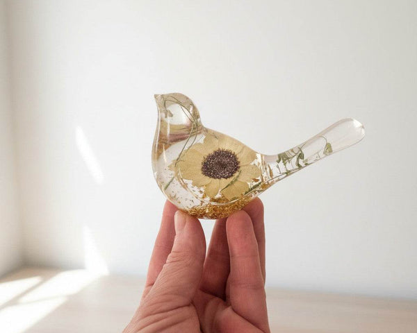 Resin bird ornament with a pressed yellow Sunflower, green botanicals, and gold leaf in a clear finish.