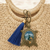 Sea turtle keychain in antique bronze with blue tassel and an ornate turtle charm holding ocean-toned resin and shell details
