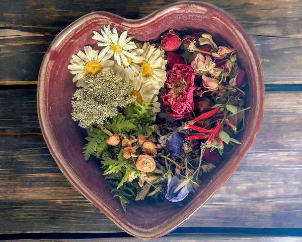 Heart-shaped ceramic bowl filled with dried flowers and herbs on a wooden surface