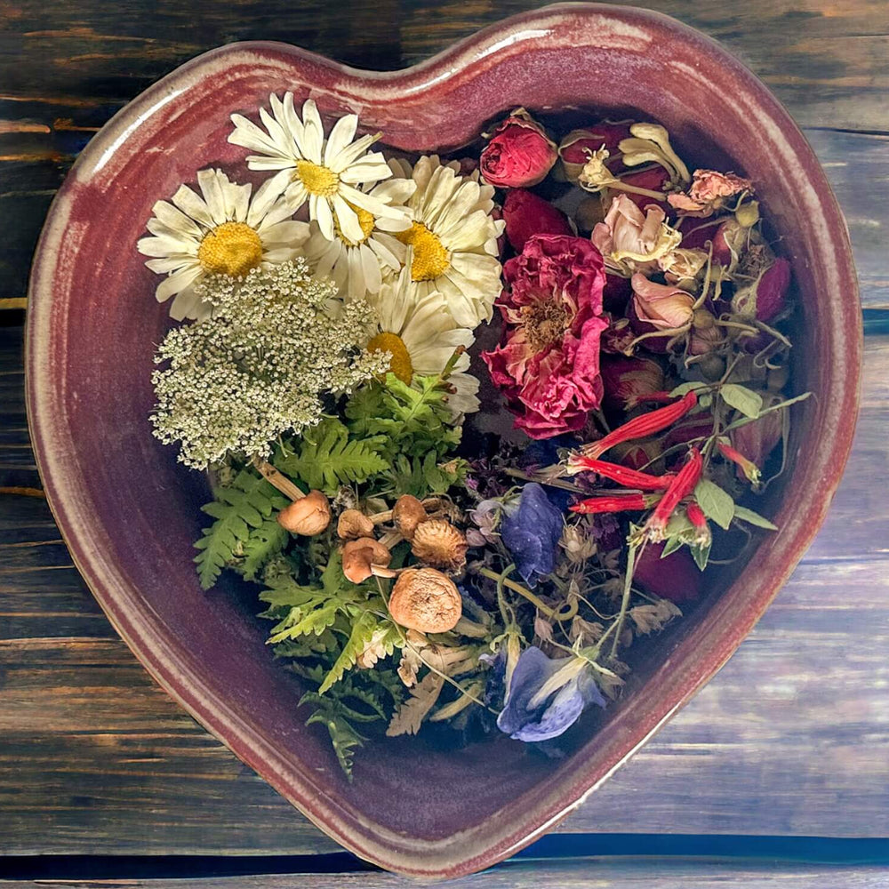 Heart-shaped ceramic bowl filled with dried flowers and herbs on a wooden surface