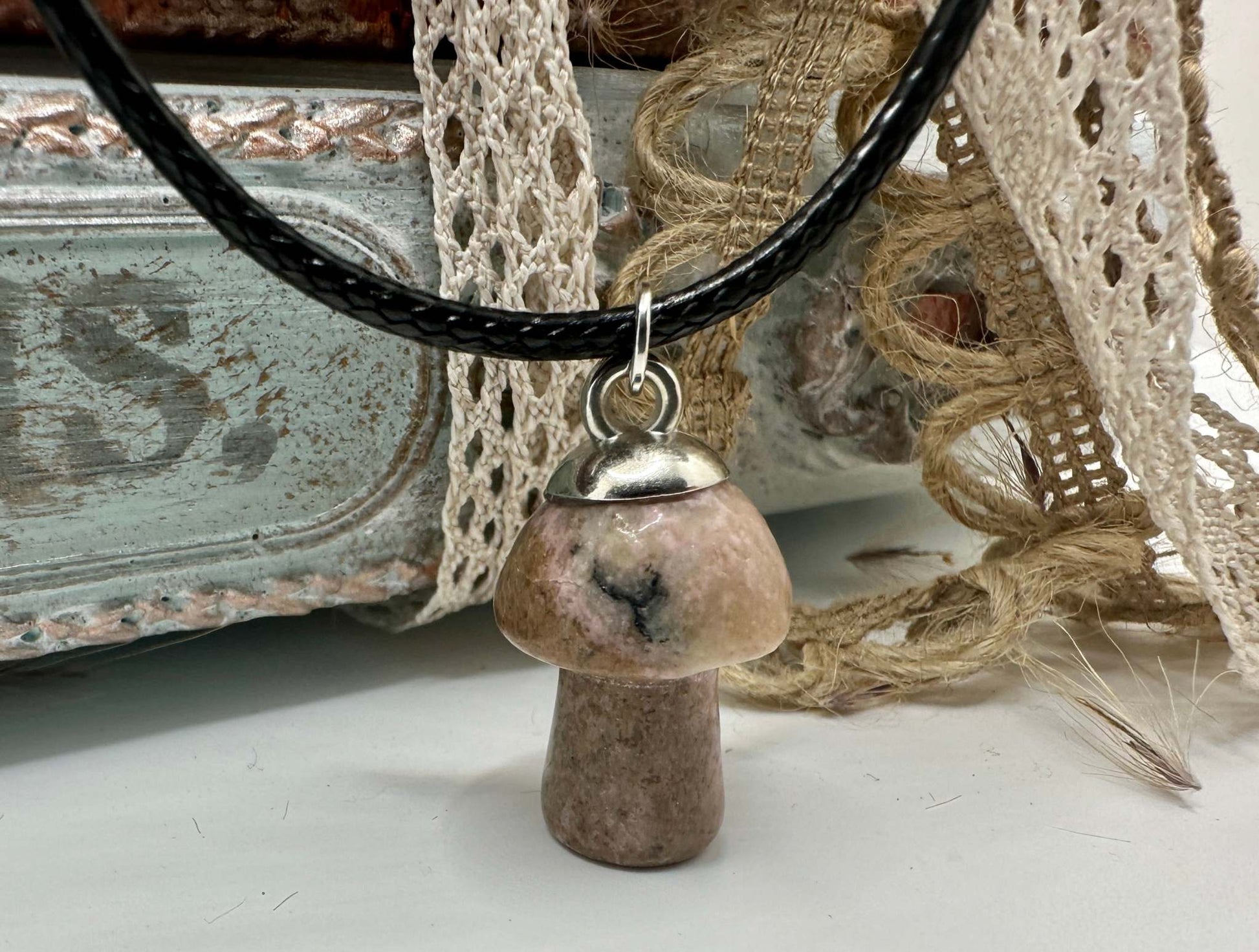 A Rhyolite mushroom shaped gemstone necklace hangs from a black leather cord